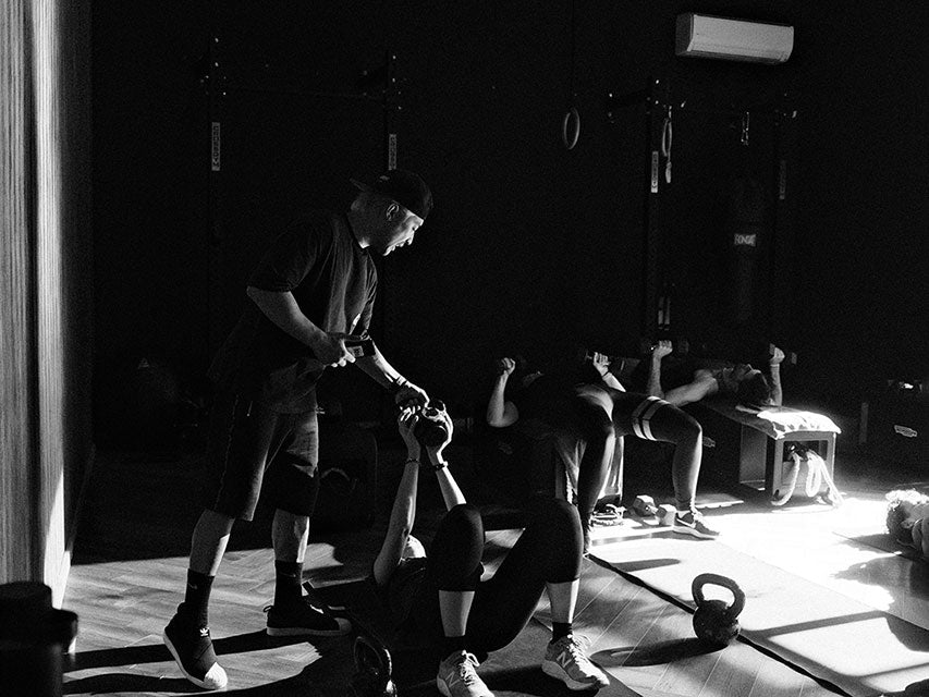 Fitness trainer Reagan holding a group fitness class using kettlebells. Photo is black and white. 